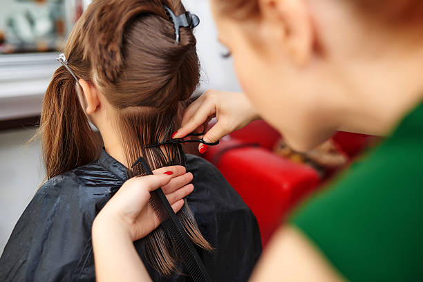 hairdresser in working day cutting hair to little girl.brown hair, rear view, holding scissor and comb.